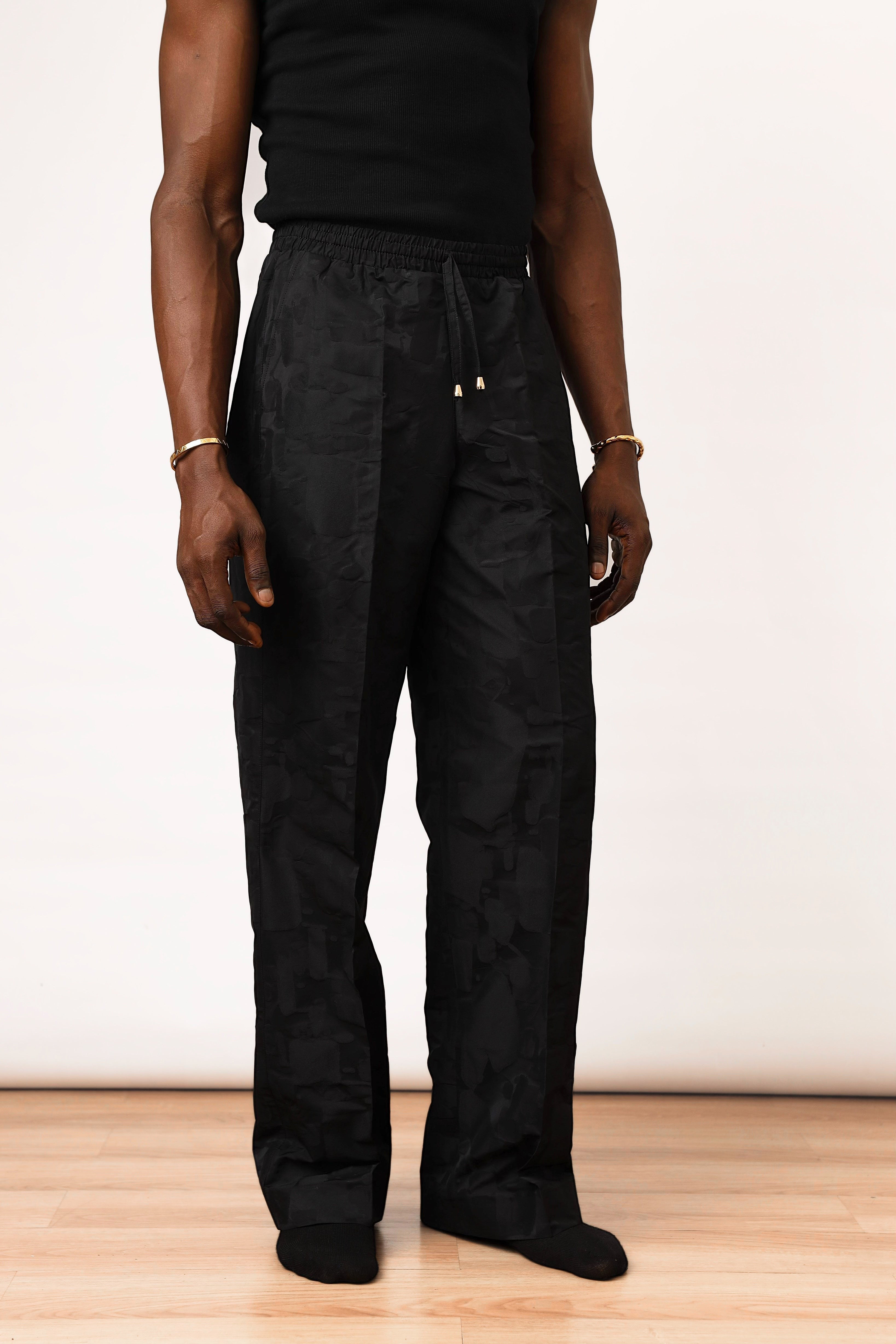 Shop Frugal black brocade trousers with a relaxed fit, drawstring waistband, and textured weave. Model wears size L.